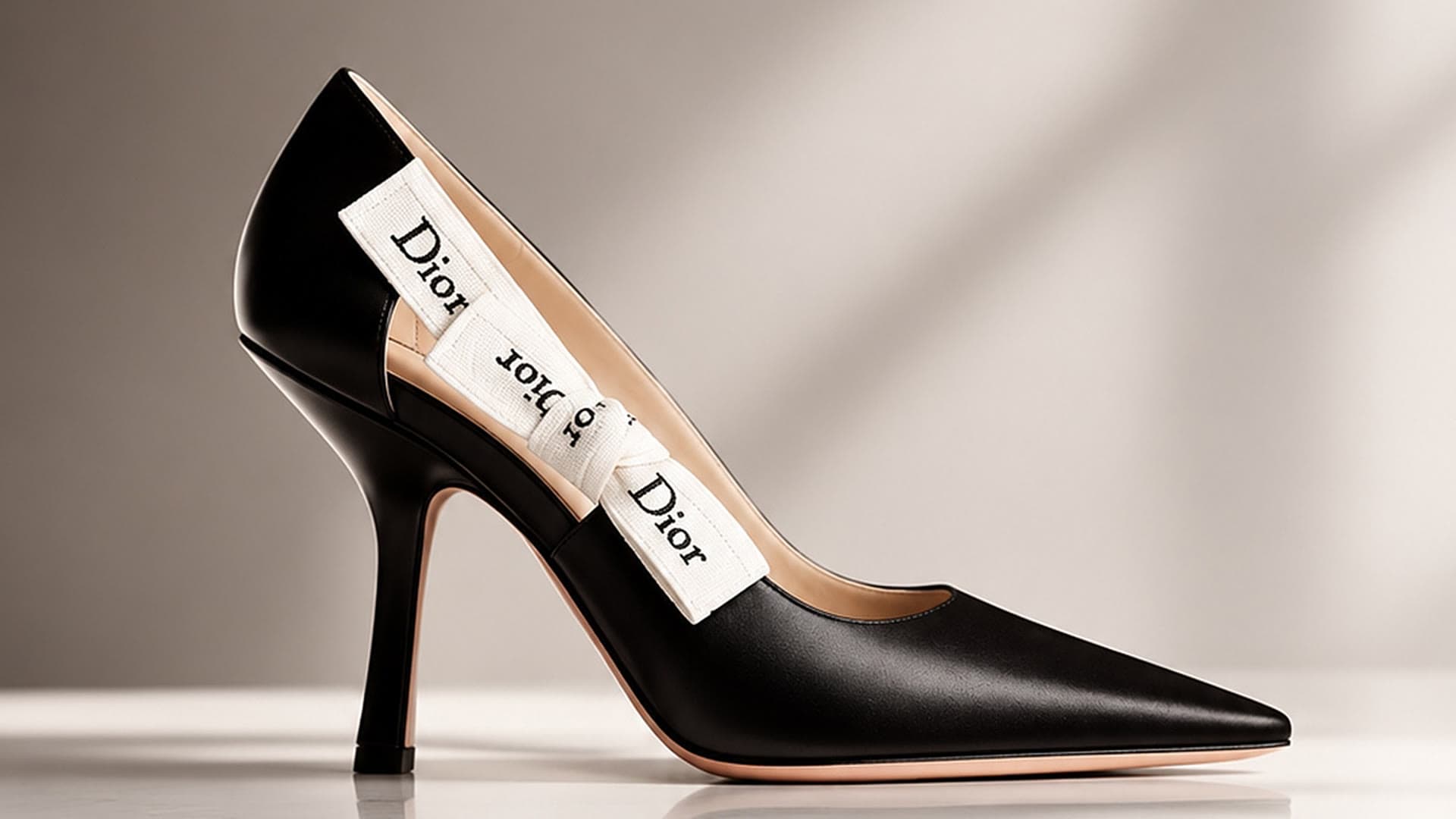 A black leather pump with a ribbon bow on a pale marble floor